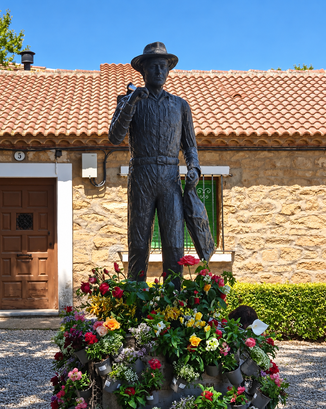 Escultura de El Colono con sombrero, rodeada de flores en Puigmoreno